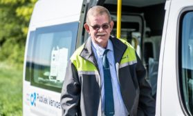 a man in a grey and yellow jacket in front of a mini bus